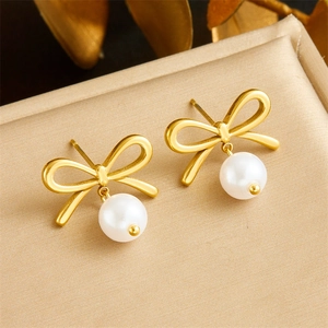 Élégantes boucles d'oreilles nœud doré avec perle sur un présentoir à bijoux beige