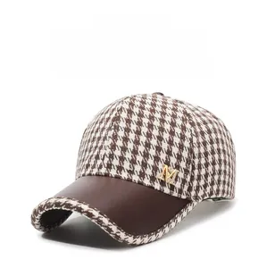 Detail of houndstooth baseball cap featuring a leather brim and gold M logo with rhinestones