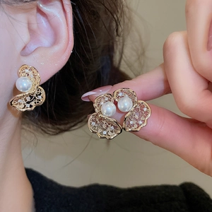 Close-up of golden hollow pearl earrings with zircon inlay on a warm background