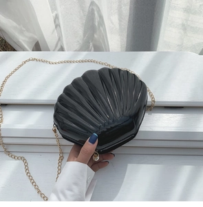 Detail of black shell-shaped evening bag with glossy texture and pearl zipper charm