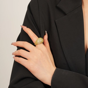 Détail d'une grande bague ovale en résine ambre avec texture marbrée verte au doigt