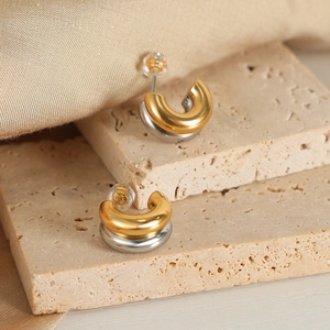 Modern two-tone C-shape hoop earrings in gold and silver plating on stone background