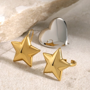 Macro shot of minimalist gold star earrings and silver heart ring on stone