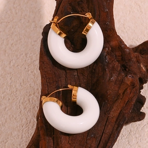 Detail of 18K gold-plated C-shape earrings with white acrylic rings on wooden prop