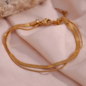 Detail of gold double-layer snake and link chain bracelet on soft pink satin fabric