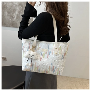 Detail of white tote bag with textured embroidery and cute cloud charm on shoulder