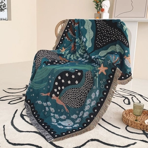 Detail of mermaid woven blanket with ocean patterns and fringe tassels on a rattan chair