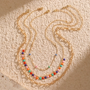 Detail of a gold layered necklace set with colorful beads on a textured stone base