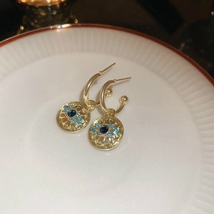 Macro detail of gold evil eye drop earrings with blue stones on a white ceramic plate