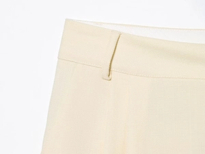 Détails du pantalon plissé beige montrant la texture du tissu et les passants de ceinture