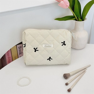Close-up of beige quilted makeup bag with black bow embroidery and Sozakka label detail