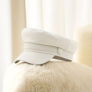 Close-up of a white PU leather newsboy cap on a soft white faux fur texture background