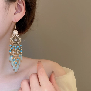 Macro shot of ethnic drop earrings with turquoise beads and golden tassels on model