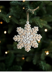 Detail of wooden snowflake Christmas ornament hanging on a pine tree with warm bokeh