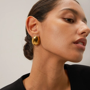 Close-up of model wearing large 18k gold plated stainless steel hammered oval earrings