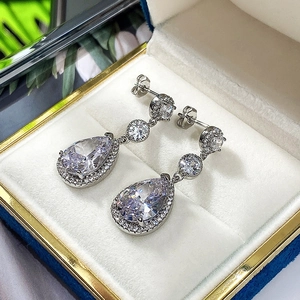Macro shot of silver teardrop earrings with AAA zircon stones on velvet cushion