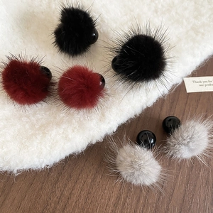 Détail de boucles d'oreilles pompon en noir, bordeaux et gris sur un support en tricot