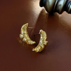 Macro shot of gold croissant-shaped stud earrings on a dark brown leather texture