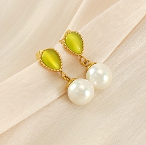 Detail of teardrop green cat eye stone and white pearl earrings on champagne fabric