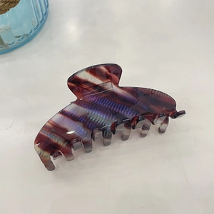 Detail of tortoiseshell acetate hair claw with purple and blue streaks on a white surface
