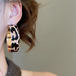 Close-up of model wearing oval leopard print leather earrings with vintage gold metal accents