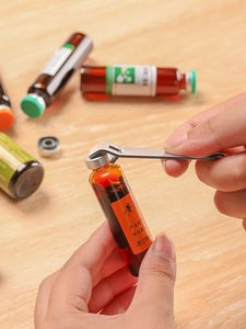 Detail showing hand using stainless steel tool to open a glass vial on a wooden desk