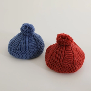 Détail de bérets en maille torsadée bleu marine et rouge rouille avec pompons doux