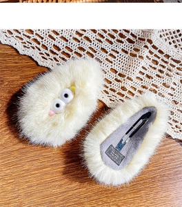 Macro detail of plush hair clip showing the metal BB clip and handmade label on wood