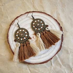 Detail of bohemian long tassel earrings with metal disc and beads on wooden background