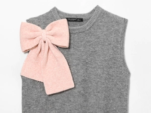 Dettaglio del gilet grigio in maglia con grande fiocco rosa e l'etichetta della taglia