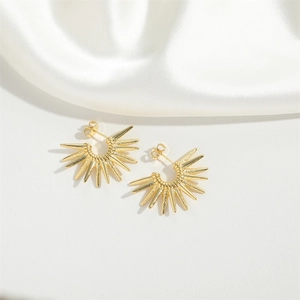 Detailed close-up of golden sunburst bow earrings on elegant white silk background