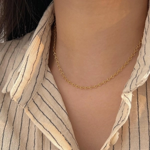 Close-up of golden heart-shaped link necklace worn by a model in a striped shirt