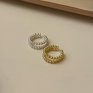 Detail view of double-row gold and silver beaded ear cuffs on a beige surface