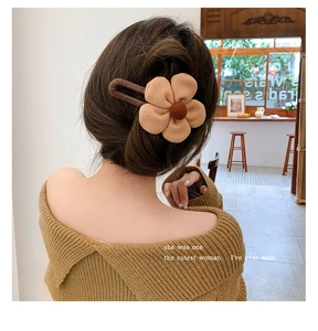 Brown fabric flower hair claw clip worn by a model in a cozy cafe setting