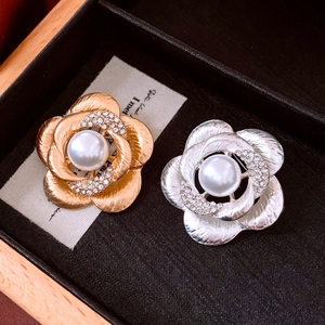 Detail view of gold and silver camellia brooches with pearls in a black jewelry box