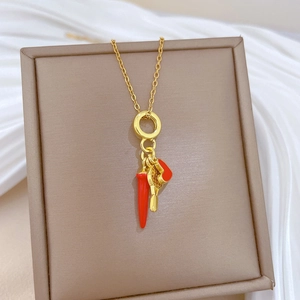 Close-up of gold-plated necklace with red chili, heart, and ring pendants in a gift box