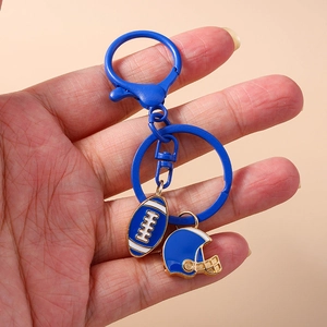 Blue rugby ball and helmet keychain charm held against a minimalist beige background