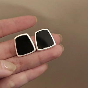 Detailed close-up of geometric silver earrings with black resin inlay held in hand