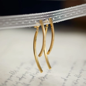 Elegant gold curved long drop earrings displayed on white lace with a vintage letter backdrop