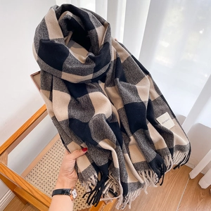 Detail of soft plaid scarf with tassels in black beige and grey on a wicker chair