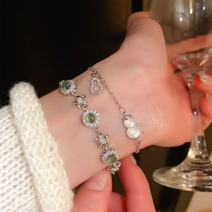 Detail of silver flower bracelet with green zircon and white gourd charm on wrist