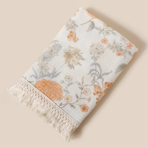 Close-up detail of a floral printed cotton baby blanket featuring delicate fringe trim.