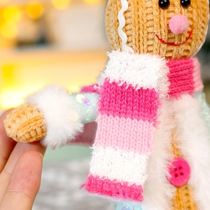 Detailed view of gingerbread man plush with knitted texture, pink scarf, and sequins