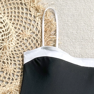 Detail of classic black one-piece swimsuit with white spaghetti straps and ruffled trim