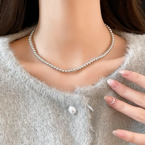 Close-up of minimalist grey pearl necklace worn with a soft grey knit cardigan