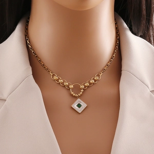 Golden geometric square necklace with green gem and white shell worn by a model