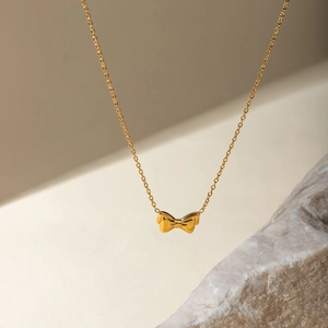 Detail of 18k gold plated stainless steel bow pendant necklace with polished finish