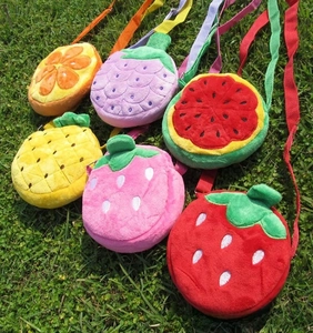 Variety of plush fruit crossbody bags for kids displayed on outdoor grass setting