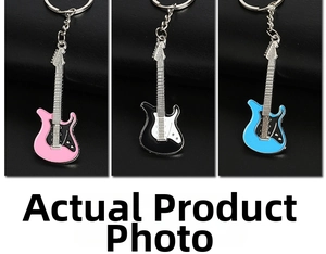 Three metal guitar keychains in pink, black, and blue enamel finish on black leather background