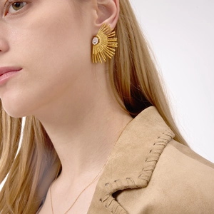 Close-up of a gold sunburst stud earring with a sparkling zircon on a female model